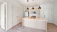 Located at 5522 Baum Blvd in Pittsburgh's Shadyside neighborhood, this modern 2-bedroom, 2-bathroom unit offers a thoughtfully designed open-concept layout. The combined kitchen and living area serves as the heart of the space, anchored by a sleek peninsula with light wood cabinetry and a quartz-style countertop. Three statement pendant lights with gold interiors hang above, adding a contemporary touch. The kitchen is equipped with stainless steel appliances, including a refrigerator, range, microwave, and dishwasher, all complemented by flat-panel cabinetry in a warm natural wood tone. Light hardwood-style flooring runs throughout, while exposed concrete ceiling accents lend an industrial character to the living area. Large floor-to-ceiling windows in the bedrooms invite abundant natural light, creating bright, airy spaces. The primary bedroom offers a comfortable footprint and direct access to an en-suite bathroom featuring a floating vanity with mirror, light tile flooring, and a glass-enclosed walk-in shower. The second bathroom includes a full soaking tub with tiled surround. A dedicated utility room and closet provide practical storage. The clean, white palette throughout gives the entire unit a crisp, contemporary feel.