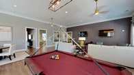 Located at 6701 Fox Rd in Raleigh, NC, this single-floor community amenity space is designed to offer residents a sophisticated and versatile gathering environment. The open layout is anchored by warm hardwood-style flooring that flows seamlessly throughout, complemented by crown molding and recessed lighting that lend a polished, upscale feel.

The main lounge area features multiple seating arrangements, including plush white sofas, accent chairs, and side tables, all oriented around wall-mounted flat-screen televisions. A deep charcoal accent wall provides a bold focal point, while large windows dressed with patterned drapery and wood blinds flood the space with natural light and offer views of the surrounding outdoor area.

A regulation-size billiards table with a rich red felt surface serves as the entertainment centerpiece of the room, illuminated by a stylish industrial-style pendant light fixture. Adjacent to the game area, a round dining table with white upholstered chairs creates an intimate gathering spot, ideal for casual meals or social events.

A separate seating alcove with leather accent chairs and an interior window provides a quieter, more private retreat within the space. The overall ambiance balances contemporary design with comfortable functionality, making it a well-appointed destination for socializing and recreation.