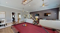Located at 6701 Fox Rd in Raleigh, NC, this single-floor community amenity space is designed to offer residents a sophisticated and versatile gathering environment. The open layout is anchored by warm hardwood-style flooring that flows seamlessly throughout, complemented by crown molding and recessed lighting that lend a polished, upscale feel.

The main lounge area features multiple seating arrangements, including plush white sofas, accent chairs, and side tables, all oriented around wall-mounted flat-screen televisions. A deep charcoal accent wall provides a bold focal point, while large windows dressed with patterned drapery and wood blinds flood the space with natural light and offer views of the surrounding outdoor area.

A regulation-size billiards table with a rich red felt surface serves as the entertainment centerpiece of the room, illuminated by a stylish industrial-style pendant light fixture. Adjacent to the game area, a round dining table with white upholstered chairs creates an intimate gathering spot, ideal for casual meals or social events.

A separate seating alcove with leather accent chairs and an interior window provides a quieter, more private retreat within the space. The overall ambiance balances contemporary design with comfortable functionality, making it a well-appointed destination for socializing and recreation.