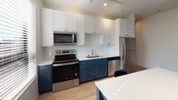 Located on Fourth Street SE in Minneapolis, this single-floor unit offers a thoughtfully designed interior with a clean, modern aesthetic. The layout, visible in the 3D overview, includes a living area, a well-appointed kitchen, multiple bedrooms, and two full bathrooms, all connected by a bright, light-filled hallway with light wood-tone flooring that flows consistently throughout the space.

The kitchen is a standout feature, combining white upper cabinetry with navy lower cabinets and a classic subway tile backsplash. Stainless steel appliances — including a refrigerator, electric range, microwave, and dishwasher — complement the white quartz countertops. A navy island with seating provides additional workspace and casual dining space. Track lighting and multiple windows allow natural light to fill the kitchen.

The living area is compact and functional, featuring a wall-mounted television, sofa, and a window with views of the surrounding Minneapolis skyline. Each bedroom includes light wood flooring, a window with blinds for natural light and privacy, and built-in or mirrored closet storage. One bedroom also includes a dedicated desk area.

Both bathrooms feature large-format tile flooring, navy vanities with gold hardware, and walk-in glass-enclosed showers, maintaining the unit's consistent two-tone design language throughout.