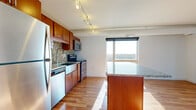 This efficiently designed 2-bedroom, 2-bathroom unit is laid out across a single floor, making smart use of its compact footprint. The open-concept kitchen and living area serves as the heart of the home, featuring warm hardwood flooring, rich cherry wood cabinetry, a mosaic tile backsplash, and a full suite of stainless steel appliances including a refrigerator, electric range, built-in microwave, and dishwasher. A granite-topped island provides additional prep and dining space. Large floor-to-ceiling windows flood the living area with natural light and offer expansive views of the surrounding landscape, while a glass door leads to a private balcony. Both bedrooms are carpeted and receive generous natural light through wide windows overlooking the outdoors. The primary bedroom includes a closet and connects to the hallway. Each bathroom features tile flooring, a cherry wood vanity with granite countertop, and a full bathtub and shower combination. Track lighting throughout the main living area adds a modern, functional touch, and exposed ductwork lends an understated industrial character to the overall aesthetic.