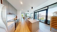 Located in Midtown Atlanta, this contemporary 2-bedroom, 2-bathroom residence offers a thoughtfully designed open-concept layout bathed in natural light. Light-toned hardwood flooring runs throughout, complementing the clean white walls and modern finishes. The kitchen serves as the centerpiece of the living area, featuring a large waterfall island with an integrated sink, warm wood cabinetry, white subway tile backsplash, and stainless steel appliances — ideal for both cooking and entertaining. The living room is defined by dramatic floor-to-ceiling windows on two sides, framing panoramic views of the Atlanta skyline and surrounding cityscape, creating a bright and airy atmosphere. A long, well-lit hallway connects the private quarters, with each bedroom offering expansive floor-to-ceiling windows that capture sweeping urban views. The primary bedroom is generously proportioned, featuring a ceiling fan and direct access to a dedicated bathroom with a dual-sink vanity, marble-style tile flooring, and an adjacent walk-in closet with open shelving. The second bathroom includes a full tub-shower combination with white subway tile and matte black fixtures. The overall design reflects a clean, modern aesthetic with warm accents throughout.