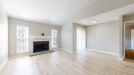 This single-floor residence offers a clean, modern aesthetic throughout, combining functional design with comfortable living spaces. The open living area serves as the heart of the home, featuring light hardwood-style flooring, neutral gray walls, and a classic fireplace with a white mantel as a central focal point. Natural light flows in through multiple windows with blinds and a sliding glass door fitted with vertical shades, providing easy access to the outdoors.

The kitchen is well-equipped and thoughtfully designed, showcasing gray shaker-style cabinetry, white quartz countertops, a classic subway tile backsplash, and a full suite of stainless steel appliances including a refrigerator, dishwasher, and electric range with overhead ventilation. A breakfast bar provides additional counter space and a natural transition between the kitchen and the main living area.

The bedrooms are carpeted in warm beige tones, each outfitted with a ceiling fan and window with blinds, creating a comfortable and well-ventilated environment. The bathroom features large-format white wall tiles surrounding a soaking tub and shower combination, with light wood-look flooring and clean chrome fixtures, conveying a crisp, refreshed finish throughout.