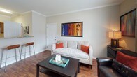This single-floor residence offers a thoughtfully designed layout with a warm, neutral color palette throughout. The kitchen is a functional highlight, featuring rich dark wood cabinetry, granite-look countertops, and stainless steel appliances including an electric range with microwave and a full-size refrigerator. Wood-look flooring ties the kitchen seamlessly into the adjacent areas.

The living area is bright and welcoming, benefiting from large windows that invite ample natural light. Crown molding adds a refined architectural touch, while warm hardwood-style flooring enhances the overall aesthetic. A dedicated seating area off the living room provides additional space for relaxing or entertaining, complete with access to natural light through multiple windows.

The bedroom is a serene retreat, carpeted for comfort and equipped with a ceiling fan. Two generously sized windows dressed with sheer curtains fill the room with soft, diffused light, creating a calm and restful atmosphere.

The full bathroom features tile flooring, a vanity with granite-look countertops and dark wood cabinetry, and a shower-tub combination. A dedicated in-unit laundry area accommodates a full-size washer and dryer, complete with overhead wire shelving for added storage convenience. Together, these spaces create a cohesive, comfortable, and practical living environment.
