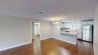Located at 45 Kings Way in Waltham, Massachusetts, this two-bedroom, one-bathroom home offers a well-organized layout with a thoughtful mix of functional spaces. The combined kitchen and living room serves as the heart of the home, featuring rich hardwood flooring and an elegant chandelier that anchors the living area. The kitchen is outfitted with white cabinetry, light countertops, stainless steel appliances including a refrigerator and dishwasher, and a window that brings in natural light and outdoor views. The open flow between the kitchen and living room creates a comfortable, connected feel throughout the main space. The primary bedroom is generously sized, with hardwood flooring and direct access to the hallway. The second bedroom features plush carpeting and a window that introduces natural light. The full bathroom includes a shower-tub combination with clean, white finishes. A dedicated laundry room with a full-size washer and dryer adds everyday convenience. The staircase, illuminated by a window, connects the levels with clean lines and bright, neutral walls. Throughout the home, soft gray-toned walls, textured ceilings, and crisp white trim contribute to a cohesive and welcoming aesthetic.