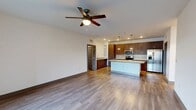 This 1,230-square-foot single-story residence offers 3 bedrooms, 2 bathrooms, and a thoughtfully designed open-concept layout. The combined kitchen and living area serves as the heart of the home, showcasing a chef-inspired kitchen equipped with rich wood-tone cabinetry, granite countertops, a large center island with pendant lighting, subway tile backsplash, and a full suite of stainless steel appliances including a refrigerator with ice maker, range, microwave, and dishwasher. The living room features warm wood-look flooring, a ceiling fan, and a sliding glass door that opens to an outdoor balcony, allowing abundant natural light. The primary bedroom measures 190 square feet and includes direct access to a dedicated closet and a private bathroom with granite vanity, wood-tone cabinetry, and wood-look tile flooring. Additional bedrooms are well-sized with natural light from windows fitted with blinds and ceiling fans. A second full bathroom mirrors the modern design found throughout. The dedicated laundry room houses a full-size washer and dryer with overhead wire shelving. Two closets provide ample storage, including a walk-in with multi-tier wire shelving. Consistent wood-look flooring and neutral walls create a cohesive, contemporary aesthetic throughout the unit.