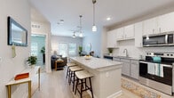 Located at 2101 Lakeview Ridge Circle in Apopka, Florida, this single-floor residence offers a thoughtfully designed open-concept layout with contemporary finishes throughout. The kitchen is a standout feature, equipped with white shaker cabinetry, granite countertops, stainless steel appliances including a refrigerator, range, and microwave, a subway tile backsplash, and a generously sized granite island with bar seating illuminated by pendant lighting. Light wood-style flooring flows seamlessly from the kitchen into the living area, which is bright and welcoming, featuring a ceiling fan, neutral-toned walls, and a glass door that opens to the outdoors, filling the room with natural light. Two well-proportioned bedrooms are finished with plush carpeting, ceiling fans, and ample natural light from windows with blinds, creating a calm and restful atmosphere. The bathroom features a granite-topped vanity with white cabinetry, a large frameless mirror, and light wood flooring for a clean, modern look. A dedicated laundry area houses a full-size Whirlpool washer and dryer alongside built-in shelving for added storage. The overall ambiance of the space is modern, bright, and functional, making it a comfortable home in the heart of Central Florida.
