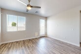 Located in Phoenix, AZ, this single-story home delivers a clean, modern aesthetic throughout its four bedrooms and three bathrooms. Wood-look plank flooring runs consistently across the living spaces, lending warmth and visual continuity to the interior. The open-concept kitchen and living area forms the heart of the home, featuring a central island with white quartz countertops, two-tone cabinetry in white and light gray, stainless steel appliances including a dishwasher and French door refrigerator, recessed lighting, and a built-in pantry with open shelving. Natural light flows in through blinded windows, complementing the neutral palette of soft gray and white walls throughout. Each bedroom is comfortably proportioned, with ceiling fans, windows with outdoor views, and consistent wood-look flooring. The spacious primary bedroom includes a walk-in closet with built-in shelving and hanging rods. The bathrooms are finished in a crisp white scheme, with one full bathroom featuring a white vanity with quartz countertop, a tub-shower combination with built-in shelving, and wood-look tile flooring. An additional half bath provides added convenience. The exterior dollhouse view reveals a backyard with a patch of artificial turf, gravel landscaping, and a block wall enclosure, offering a low-maintenance outdoor retreat ideal for the Arizona climate.