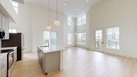 Located at 700 E. Long St. in Columbus, Ohio, this thoughtfully designed one-bedroom, two-bathroom unit offers a bright and modern living experience across a single floor. The open-concept living and kitchen area is the centerpiece of the home, boasting dramatically high ceilings with clerestory windows that flood the space with natural light. Large windows frame views of the surrounding Columbus skyline, enhancing the airy atmosphere. Light wood-tone flooring flows seamlessly throughout the main living areas, complementing the clean, neutral color palette.

The kitchen is well-appointed with gray shaker-style cabinetry, white subway tile backsplash, stainless steel appliances, and a spacious peninsula with a built-in sink — ideal for both cooking and entertaining. Globe pendant lights add a modern, stylish touch overhead.

The generously sized primary bedroom features soft carpeting, a large window with city views, and direct access to an en suite bathroom. The en suite bathroom includes a glass-enclosed shower, a teal vanity with sleek black hardware, and light wood flooring. A second bathroom offers a warm wood vanity and similarly clean finishes. A dedicated closet and hallway complete this well-organized, contemporary home.