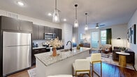This thoughtfully designed one-bedroom, one-bathroom residence in Lewisville, TX offers a modern open-concept layout that maximizes every inch of its single-floor plan. Rich hardwood-style flooring flows throughout, anchoring each space with warmth and continuity.

The kitchen is a standout, featuring dark espresso cabinetry, a classic subway tile backsplash, stainless steel appliances including a full-size refrigerator and microwave, and a granite-topped island with a black matte sink. Pendant lighting above the island adds a stylish focal point, while the open sightline connects the kitchen directly to the living area, creating an ideal space for entertaining. A dedicated pantry provides additional storage.

The living room is bright and inviting, with a ceiling fan, large windows, and a glass-paned door that ushers in natural light. The bedroom offers a comfortable retreat with windows overlooking greenery, a ceiling fan, and two closets for ample storage.

The bathroom continues the granite countertop theme with a dark wood vanity, a large mirror, and hardwood-style flooring. A walk-in closet is conveniently accessible directly from the bathroom, enhancing functionality. The overall palette of neutral tones and contemporary finishes gives the entire residence a clean, cohesive aesthetic.