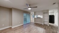 Located at 701 West Longspur Boulevard in Austin, TX, this well-appointed two-bedroom, two-bathroom residence offers a practical and comfortable single-floor layout. The open living room is finished with warm wood-style luxury vinyl flooring that continues throughout the home, and features a ceiling fan with integrated lighting. A sliding glass door dressed with vertical blinds fills the space with natural light and provides outdoor access. Built-in open shelving between the living area and kitchen adds functional display and storage space. The galley-style kitchen is equipped with white cabinetry, dark granite-style countertops, a double basin sink, and black appliances including a refrigerator and range. Both bedrooms are comfortably sized, each outfitted with a ceiling fan and large closet. The primary bedroom offers generous proportions with ample room for furniture arrangement. The two bathrooms are finished consistently with wood-style flooring, gray vanities topped with dark countertops, and tub-shower combinations with tile surrounds. A dedicated laundry area adds everyday convenience. Neutral gray wall tones and clean white trim tie the entire home together in a cohesive, move-in-ready aesthetic.