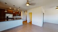 This single-floor unit showcases a thoughtfully designed open-concept layout that seamlessly connects the living area and kitchen. The kitchen is a standout feature, equipped with rich walnut-toned cabinetry, dark countertops, and a full suite of stainless steel appliances including a French door refrigerator, electric range, and over-the-range microwave. A white subway tile backsplash adds a clean, contemporary contrast to the warm cabinetry tones. A peninsula with an undermount sink extends into the living space, creating a natural division while maintaining an open, airy feel. Pendant lighting hangs above the peninsula, while recessed lighting and a ceiling fan illuminate the broader living area. Wood-look plank flooring runs throughout the unit, providing a warm and cohesive aesthetic. A large window in the living area frames an outdoor view of greenery, allowing natural light to fill the space. The bedroom is a calm, neutral retreat featuring a ceiling fixture and a reach-in closet. The bathroom is cleanly finished with a tiled tub-shower surround, dark-toned vanity with an undermount sink, and matching wood-look flooring, completing the unit's consistent modern design palette.
