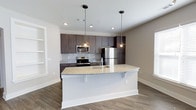 Located at 100 Underwood Dr in Summerville, South Carolina, this single-floor residence offers a thoughtfully designed living space with modern finishes throughout. The open-concept kitchen serves as a focal point of the home, centered around a generous island topped with light granite countertops and an undermount sink, illuminated by a pair of industrial-style pendant lights. Dark espresso-toned cabinetry extends to the upper walls, providing ample storage while creating a striking contrast against the light granite surfaces and classic subway tile backsplash. The kitchen is equipped with a full suite of stainless steel appliances, including a French door refrigerator, electric range, and built-in microwave. Recessed ceiling lighting adds to the bright, welcoming atmosphere. The flooring throughout features durable wood-look planks in a warm neutral tone, tying the space together seamlessly. Clean white walls and crisp trim work complement the contemporary aesthetic, creating an inviting and functional environment. The layout flows naturally, making the space well-suited for both everyday living and entertaining.