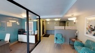 This single-floor professional office space is thoughtfully designed to create a welcoming and functional environment. The layout is divided into distinct zones, each serving a specific purpose while maintaining a cohesive aesthetic throughout.

Upon entry, visitors are greeted by a well-appointed reception area featuring light tile flooring and a reception desk with a decorative patterned partition. The desk area is finished with a warm wood-toned countertop and is positioned to provide staff with clear visibility of the entrance. Recessed and flush-mounted ceiling fixtures provide consistent, even lighting throughout the space.

The waiting area is furnished with stylish teal patterned chairs arranged to encourage comfortable seating, complemented by small side tables and framed abstract artwork on the walls. A potted plant adds a natural touch to the contemporary setting. The color palette — featuring teal accents against neutral gray and white walls — creates a calm yet modern atmosphere.

A glass-partitioned private office, framed with sleek black metal, offers a separate workspace while maintaining visual openness. This area is furnished with a desk and storage cabinetry, with teal accent walls adding design continuity. The overall ambiance is professional, clean, and inviting, well-suited for client-facing operations.