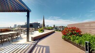 Located at 355 Broad St in Newark, NJ, this rooftop terrace is a thoughtfully designed outdoor amenity space offering a rich blend of hardscape and landscape elements. The terrace is organized into several distinct zones, each serving a different function while maintaining a cohesive aesthetic throughout.

A combination of composite wood decking and large-format stone pavers defines the circulation and gathering areas, lending a clean, modern character to the space. Raised planter beds and garden borders are filled with vibrant red flowering plants, lush ornamental grasses, and seasonal greenery, adding natural color and texture across the roofline.

Multiple seating areas are distributed throughout the terrace, including sections shaded by sleek steel pergolas that provide partial coverage and architectural definition. Cushioned lounge chairs, outdoor sofas, and café-style dining sets accommodate both relaxed lounging and social gatherings. A dedicated lawn area with artificial turf and sun loungers offers an additional recreational zone.

Glass panel railings line the perimeter of the terrace, ensuring unobstructed panoramic views of the Newark skyline, including a notable historic church steeple and surrounding urban landscape. The open-air design allows for abundant natural light throughout the day. This rooftop space presents a well-appointed urban retreat in the heart of Newark.