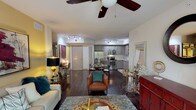 This well-appointed single-floor residence offers a thoughtfully designed open-concept layout that seamlessly connects the living, dining, and kitchen areas. Rich dark hardwood flooring extends throughout the main living spaces, anchoring the warm, eclectic aesthetic. The living room is generously sized, featuring a ceiling fan, sliding glass door access to the outdoors, and ample room for multiple seating arrangements. Bold artwork and layered lighting enhance the inviting atmosphere.

The kitchen is outfitted with stainless steel appliances, including a French door refrigerator, electric range, and dishwasher. Gray wood-grain cabinetry pairs with granite-style countertops and a classic white subway tile backsplash, offering both style and functionality. A glass-top dining table sits just adjacent, with a stacked washer and dryer conveniently tucked nearby.

Two bedrooms provide comfortable retreats. The primary bedroom features teal accent walls, a window with natural light, and warm hardwood flooring. The second bedroom also benefits from multiple windows and hardwood floors. Both bathrooms are finished with granite vanities, tiled tub-shower combinations, and wood-framed mirrors, maintaining a cohesive, modern design throughout.