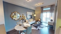 This thoughtfully designed Dallas residence offers a seamless blend of modern aesthetics and functional living across a single floor. The open-concept living and dining area serves as the heart of the home, featuring rich hardwood-style flooring, a striking slate-blue accent wall, and track lighting overhead. A glass sliding door floods the space with natural light and provides access to an outdoor balcony, while a compact dining table with teal chairs anchors the dining nook alongside a decorative gold-framed mirror. The kitchen is outfitted with crisp white shaker cabinetry, glass-front upper cabinets, a textured stone tile backsplash, sage green countertops, and stainless steel appliances, including a smooth-top range and over-the-range microwave. Both bedrooms are carpeted and bathed in natural light from large windows offering views of the surrounding Dallas cityscape and greenery. Each room features ceiling fans and is accented with tasteful decor, including gold sunburst wall art and bold navy drapery. The bathroom is well-appointed with a dual-function glass-enclosed shower and soaking tub, a wide vanity with dark countertops, recessed lighting, and direct access to a spacious walk-in closet. Throughout, the residence maintains a cohesive contemporary style with warm gold accents and neutral tones.