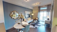 This thoughtfully designed Dallas residence offers a seamless blend of modern aesthetics and functional living across a single floor. The open-concept living and dining area serves as the heart of the home, featuring rich hardwood-style flooring, a striking slate-blue accent wall, and track lighting overhead. A glass sliding door floods the space with natural light and provides access to an outdoor balcony, while a compact dining table with teal chairs anchors the dining nook alongside a decorative gold-framed mirror. The kitchen is outfitted with crisp white shaker cabinetry, glass-front upper cabinets, a textured stone tile backsplash, sage green countertops, and stainless steel appliances, including a smooth-top range and over-the-range microwave. Both bedrooms are carpeted and bathed in natural light from large windows offering views of the surrounding Dallas cityscape and greenery. Each room features ceiling fans and is accented with tasteful decor, including gold sunburst wall art and bold navy drapery. The bathroom is well-appointed with a dual-function glass-enclosed shower and soaking tub, a wide vanity with dark countertops, recessed lighting, and direct access to a spacious walk-in closet. Throughout, the residence maintains a cohesive contemporary style with warm gold accents and neutral tones.