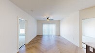 This well-designed single-floor residence offers a cohesive blend of modern finishes and functional living spaces. The open living area makes an immediate impression with its striking herringbone-patterned hardwood flooring, crisp white walls, and a ceiling fan with integrated lighting. A large sliding glass door fitted with vertical blinds fills the room with natural light and provides access to the outdoors. The kitchen is a standout feature, showcasing rich dark-toned cabinetry, light granite countertops, a sparkling mosaic tile backsplash, and a full suite of stainless steel appliances including a range, microwave, refrigerator, and dishwasher. A central island with pendant lighting adds both workspace and visual appeal. The herringbone flooring continues seamlessly from the living area into the kitchen, reinforcing a sense of continuity. The bedrooms feature plush neutral carpeting and generous windows fitted with roller shades, offering views of the surrounding urban rooftops and cityscape. Additional rooms with light hardwood flooring provide flexible living or workspace options. The bathroom is appointed with patterned tile flooring, a dark-toned vanity with stone countertop, and matte black hardware accents, adding a refined touch to the overall design.
