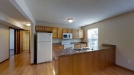 Located at 1 Hidden Brooke Way in Culloden, West Virginia, this single-floor home offers a functional and welcoming layout designed for comfortable everyday living. The open-concept floor plan connects the living area and kitchen seamlessly, creating a spacious and airy feel throughout. The living area features soft carpeting, neutral-toned walls, and a ceiling fan that adds both comfort and style. Warm wood-toned interior doors and trim provide a cohesive design element throughout the home. The kitchen is well-appointed with honey-toned wooden cabinetry offering generous storage, dark laminate countertops, and a suite of white appliances including a refrigerator, electric range, and built-in microwave. A peninsula with an integrated sink and breakfast bar extends into the living space, making it ideal for casual dining or entertaining. Light hardwood flooring runs through the kitchen and into the connected living areas, adding warmth and easy maintenance. Multiple windows allow natural light to filter in, brightening the interior and providing views of the surrounding greenery. The overall ambiance is clean, practical, and move-in ready, making this home a solid choice in the Culloden area.