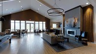 This elegantly designed single-floor space makes an immediate impression with its dramatic vaulted ceilings that soar overhead, creating an expansive and airy atmosphere. A striking double-ring chandelier serves as the centerpiece of the main lounge area, casting warm ambient light across the open-plan layout. The lounge is anchored by a plush sectional sofa, paired with stylish accent tables and area rugs that define the seating zone, all set atop warm hardwood flooring that runs throughout the space.

A sleek, floor-to-ceiling fireplace with a modern linear design adds both warmth and architectural interest to one wall, complemented by curated wall art above. Adjacent to the lounge, a casual dining area features tables and chairs bathed in natural light from large floor-to-ceiling windows and glass doors that open to an outdoor space, blending the interior with its surroundings.

Further into the space, a well-appointed kitchenette or bar area is visible, featuring dark cabinetry, pendant lighting, and a clean countertop layout. The rich contrast between the deep brown accent walls and crisp white ceiling elements adds depth and sophistication, while recessed lighting throughout ensures the space remains bright and welcoming at all times.