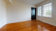 Located at 801 N Arthur Ashe Blvd in Richmond, Virginia, this single-floor unit offers a thoughtfully laid-out living space with classic charm and practical amenities. Warm, polished hardwood floors extend throughout the main living areas and bedrooms, lending a timeless character to the interior. The entry welcomes visitors through a bold black front door accompanied by a side window that invites natural light into the space.

The living and common areas feature clean white walls, generous baseboards, and arched architectural details visible in the floor plan, adding a touch of traditional design. Multiple windows fitted with blinds bring in natural light and offer views of the surrounding brick streetscape.

The kitchen is efficiently designed with white cabinetry — including glass-front upper cabinets — dark granite-style countertops, a gas range, and a stainless steel sink. A stacked washer and dryer unit is conveniently integrated directly into the kitchen area. A microwave and open shelving complete the functional layout.

The bathroom features a striking black-and-white checkered tile floor, providing a classic aesthetic contrast to the surrounding hardwood flooring. A window in the bathroom allows for natural ventilation and light.

The bedrooms are bright and well-proportioned, each with hardwood floors, ceiling fixtures, and windows overlooking the neighboring brick exterior, creating a cozy urban atmosphere throughout.