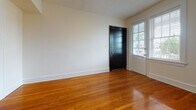 Located at 801 N Arthur Ashe Blvd in Richmond, Virginia, this single-floor unit offers a thoughtfully laid-out living space with classic charm and practical amenities. Warm, polished hardwood floors extend throughout the main living areas and bedrooms, lending a timeless character to the interior. The entry welcomes visitors through a bold black front door accompanied by a side window that invites natural light into the space.

The living and common areas feature clean white walls, generous baseboards, and arched architectural details visible in the floor plan, adding a touch of traditional design. Multiple windows fitted with blinds bring in natural light and offer views of the surrounding brick streetscape.

The kitchen is efficiently designed with white cabinetry — including glass-front upper cabinets — dark granite-style countertops, a gas range, and a stainless steel sink. A stacked washer and dryer unit is conveniently integrated directly into the kitchen area. A microwave and open shelving complete the functional layout.

The bathroom features a striking black-and-white checkered tile floor, providing a classic aesthetic contrast to the surrounding hardwood flooring. A window in the bathroom allows for natural ventilation and light.

The bedrooms are bright and well-proportioned, each with hardwood floors, ceiling fixtures, and windows overlooking the neighboring brick exterior, creating a cozy urban atmosphere throughout.