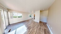 This well-appointed single-floor unit offers a clean, functional layout designed for comfortable everyday living. The spacious main living area is immediately welcoming, featuring warm wood-look plank flooring that extends throughout the common spaces, neutral-toned walls, and a ceiling fan overhead. Large windows along the perimeter flood the room with abundant natural light, offering views of surrounding greenery. The open layout provides a generous sense of space and versatility.

The kitchen is efficiently designed in a U-shaped configuration, outfitted with warm honey-toned wood cabinetry, rich dark granite countertops, and white appliances including a range, dishwasher, and refrigerator. A window above the sink brings in natural light, enhancing the workspace.

The bedrooms are carpeted for comfort and feature neutral walls and windows that look out to the exterior. Several bedrooms include built-in closets with shelving and hanging rods, providing ample storage. One bedroom benefits from a particularly generous closet with dedicated shelving units alongside a standard hanging section.

Additional spaces visible in the floor plan include a bathroom and a laundry area, rounding out the home's practical amenities. Throughout the unit, the consistent use of light, neutral tones and clean finishes creates a calm, cohesive ambiance.