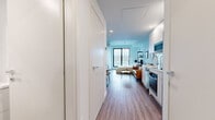 Located at 1001 Lucien-L'Allier in the heart of Montréal, this efficiently designed one-bedroom, one-bathroom unit offers a thoughtful open-concept layout that maximizes every square foot. Warm hardwood-style flooring runs throughout the main living area, anchoring the space with a clean, contemporary aesthetic. The living area comfortably accommodates a seating arrangement alongside a compact dining nook, all flowing seamlessly into a well-appointed kitchenette. The kitchen features white cabinetry, stainless steel appliances including a built-in oven and microwave, and a sleek countertop with an integrated sink — all finished to a modern standard. The bedroom is a bright, serene retreat highlighted by a floor-to-ceiling window with sliding access that frames a stunning panoramic view of the Montréal skyline and surrounding hills, filling the room with generous natural light. The bathroom is finished with large-format neutral tiles and includes a glass-enclosed walk-in shower with chrome fixtures, delivering a polished and functional space. Crisp white walls, recessed lighting, and a consistent modern palette throughout create a cohesive, airy ambiance well-suited to urban living in one of Montréal's most central neighbourhoods.