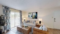 Located at 6075 Grelot Rd in Mobile, Alabama, this single-floor residence offers a well-organized and comfortable layout designed for everyday living. The open living area is a welcoming focal point, featuring wood-look flooring, a cozy fireplace, and a sliding glass door dressed with bold patterned curtains that invite natural light and provide access to an outdoor area. The space flows seamlessly into a dedicated dining area, making it ideal for both relaxing and entertaining. The kitchen is equipped with wood cabinetry, black appliances including a refrigerator, electric range, and built-in microwave, along with light-toned countertops and easy-care flooring. The bedrooms are carpeted for comfort and feature large windows with natural light. The primary bedroom is generously sized with room for substantial furnishings and is complemented by a walk-in closet offering ample storage. Additional bedrooms are well-proportioned and also include closet access. The bathroom features a single vanity with wood cabinetry, a large mirror, and a combined tub and shower, finished with clean, neutral tones and wood-look flooring. Throughout the space, textured ceilings and a light, neutral color palette create a bright, cohesive ambiance.