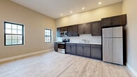 Located at 704 Eighth St in Niagara Falls, NY, this single-floor unit offers a clean, contemporary design with consistent light wood-tone vinyl flooring and neutral warm-beige walls throughout. The open kitchen is a standout feature, showcasing dark espresso-stained shaker cabinetry, a marble-look tile backsplash, light countertops, and a full suite of stainless steel appliances including a refrigerator, range, and microwave. Recessed lighting illuminates the kitchen and adjacent open living area, which benefits from natural light through black-framed windows. The generously proportioned living space is further enhanced by a wall-mounted mini-split HVAC unit, ensuring year-round comfort. Multiple additional rooms offer flexible use, each featuring the same durable flooring, tall ceilings, and black-framed windows that bring in natural light and outdoor views. A bold dark entry door with modern hardware adds a striking contrast to the light interior palette. The bathroom is thoughtfully appointed with marble-patterned tile surrounding a soaking tub, a modern floating vanity, and coordinating flooring, creating a clean and elegant finish. Overall, the space presents a fresh, move-in-ready aesthetic well suited for comfortable everyday living.