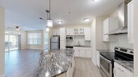 This single-floor, 3-bedroom, 2-bathroom residence offers a thoughtfully designed layout with a clean, neutral aesthetic throughout. The open-concept kitchen is a standout feature, showcasing striking granite-topped island with pendant lighting overhead, crisp white cabinetry with glass-front accents, stainless steel appliances including a refrigerator, range, and built-in microwave, plus a wall-mounted range hood. Light wood-look flooring extends through the kitchen and living areas, creating a seamless flow.

The living room is bright and airy, benefiting from natural light through large windows and a sliding glass door that opens to a private balcony overlooking lush greenery. A ceiling fan adds comfort to the space.

The three bedrooms feature plush carpeting and windows with views of the surrounding landscape, offering a calm and restful atmosphere. The primary bedroom includes access to a dedicated bathroom.

Both bathrooms are finished with large-format tile flooring and tile-surround soaking tubs, complemented by white vanities with granite countertops. A dedicated closet and hallway provide practical storage and circulation. Throughout, neutral warm-toned walls and consistent finishes contribute to a cohesive, move-in-ready environment.