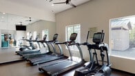 Located at 1710 NE Multnomah St in Portland, Oregon, this fitness center is a well-appointed, single-floor facility designed to support a comprehensive range of workout routines. The open floor plan is finished with durable rubber flooring and benefits from abundant natural light streaming through multiple windows, creating an energizing and inviting atmosphere throughout.

The cardio zone is anchored by a row of TRUE brand treadmills and elliptical machines, neatly lined along a full-length wall mirror that enhances the sense of space. Multiple ceiling fans are distributed throughout, ensuring consistent air circulation during workouts. Mounted flat-screen televisions provide entertainment options for cardio sessions.

The strength and functional training area offers a diverse selection of equipment, including a cable cross machine, an adjustable weight bench, a freestanding Century punching bag, medicine balls, resistance bands, and a dedicated Training Zone functional fitness rack stocked with suspension trainers and free weights. This section is ideal for dynamic, full-body training.

Recessed lighting complements the natural light, keeping the space bright at all times. A glass-enclosed laundry room is conveniently integrated into the facility, housing multiple stacked washer and dryer units. Overall, the fitness center provides a clean, modern, and thoroughly equipped environment suited for a wide variety of fitness goals.