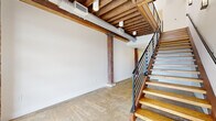 This two-story, 3-bedroom, 3-bathroom space masterfully combines industrial heritage with contemporary design. The lower level sets a striking tone with polished concrete floors, exposed wooden ceiling beams, visible ductwork, and a bold staircase featuring wood treads and a sleek black metal railing — all elements that give the space a distinctive loft character.

The upper level is the heart of the home, where warm hardwood floors and expansive exposed brick walls create an inviting, textured atmosphere. The open-plan kitchen and living area is a standout, boasting soaring ceilings with industrial-style pendant lighting, white shaker cabinetry, dark stone countertops, stainless steel appliances, and a sage-green island that serves as both a functional workspace and a visual focal point. Natural light pours in through large windows set within the brick walls.

The three bedrooms offer comfortable proportions, with the primary bedroom providing a generous layout alongside a well-appointed closet. The bathrooms are finished with neutral tile flooring, white vanities with dark stone countertops, and clean, understated fixtures. Throughout the upper floor, exposed brick accents and hardwood flooring maintain a cohesive aesthetic, connecting each room in a warm, industrial-modern narrative.