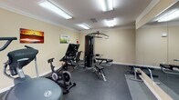 Located at 3300 Alden Pond Ln in Eagan, Minnesota, this fitness center offers a well-equipped, single-floor exercise space designed to support a well-rounded workout routine. The room features neutral beige walls accented with crown molding and a textured ceiling, creating a clean and functional environment. Durable rubber flooring covers the entire space, providing safety and comfort during exercise.

The facility is outfitted with a diverse range of equipment to accommodate both cardio and strength training. Cardio options include a treadmill, an elliptical trainer, and a stationary spin bike, while a stair-stepper rounds out the aerobic offerings. For strength training, a Life Fitness multi-station cable machine serves as the centerpiece, complemented by an adjustable weight bench and additional resistance equipment. A large wall-mounted mirror along one side of the room enhances the sense of space and allows users to monitor their form during workouts.

Bright overhead fluorescent lighting ensures the space is well illuminated throughout, and a window along one wall brings in natural light while offering a view of the outdoor surroundings. A wall-mounted television and a clock add convenience for users. Motivational artwork displayed on the walls contributes to an encouraging atmosphere. The space is also equipped with a fire safety device, reflecting attention to occupant safety.
