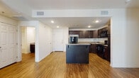 This single-floor residence offers a thoughtfully designed open-concept layout that seamlessly connects the main living areas. The kitchen serves as the centerpiece, showcasing rich, dark espresso-toned cabinetry that extends to the ceiling for ample storage, complemented by granite-style countertops and a full suite of black appliances including a refrigerator, range, and over-the-range microwave. A substantial kitchen island provides additional counter space and functions as a natural dividing point between the kitchen and the main living area. Warm hardwood-style flooring flows throughout the kitchen and living spaces, adding a sense of continuity and warmth to the open floor plan. Recessed lighting illuminates the common areas with a clean, modern look. The bedrooms are finished with plush wall-to-wall carpeting and each features a ceiling fan with a window that allows for natural light. The unit includes two full bathrooms, each outfitted with hardwood-style flooring, dark vanity cabinetry with matching granite-style countertops, and a soaking tub with an overhead shower. The overall design balances practical functionality with a cohesive, contemporary aesthetic throughout.
