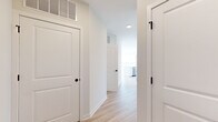 Located on the sixth floor at 100 Avenue G in Bayonne, NJ, this well-appointed 2-bedroom, 2-bathroom residence offers a bright, modern living experience. The open-concept kitchen and living area serves as the heart of the home, where a large white quartz island with an integrated sink anchors the space. The kitchen is outfitted with stainless steel appliances, including a French door refrigerator, electric range, built-in microwave, and dishwasher, complemented by a two-tone cabinet scheme of white and natural wood-grain finishes set against a clean subway tile backsplash. Light wood-tone flooring flows seamlessly throughout the unit, enhancing the airy, contemporary feel. The expansive living area is bathed in natural light from a bank of large windows offering sweeping panoramic views of the Bayonne skyline and surrounding landscape. The spacious primary bedroom enjoys its own generous window framing open outdoor views, while the second bedroom is equally well-lit. Both bathrooms are finished with light wood vanities, white quartz countertops, LED-backlit mirrors, and tiled shower surrounds. A dedicated closet provides additional storage, and a well-connected hallway ties the layout together efficiently.