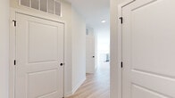 Located on the sixth floor at 100 Avenue G in Bayonne, NJ, this well-appointed 2-bedroom, 2-bathroom residence offers a bright, modern living experience. The open-concept kitchen and living area serves as the heart of the home, where a large white quartz island with an integrated sink anchors the space. The kitchen is outfitted with stainless steel appliances, including a French door refrigerator, electric range, built-in microwave, and dishwasher, complemented by a two-tone cabinet scheme of white and natural wood-grain finishes set against a clean subway tile backsplash. Light wood-tone flooring flows seamlessly throughout the unit, enhancing the airy, contemporary feel. The expansive living area is bathed in natural light from a bank of large windows offering sweeping panoramic views of the Bayonne skyline and surrounding landscape. The spacious primary bedroom enjoys its own generous window framing open outdoor views, while the second bedroom is equally well-lit. Both bathrooms are finished with light wood vanities, white quartz countertops, LED-backlit mirrors, and tiled shower surrounds. A dedicated closet provides additional storage, and a well-connected hallway ties the layout together efficiently.