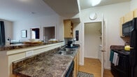 This single-floor unit offers a practical and comfortable layout across several well-defined living spaces. The kitchen features dark granite-style countertops, a double-basin sink, light wood cabinetry, and black appliances including a refrigerator, range, and microwave. Wood-style flooring runs throughout the kitchen, which connects directly to a dedicated in-unit laundry closet housing a full-size washer and dryer.

The living room is bright and inviting, with a large sliding glass door that opens to a private balcony and provides views of the surrounding greenery. Wood-style flooring continues here, complementing the open, airy feel of the space.

Multiple bedrooms offer carpeted floors and unique accent wall colors, creating distinct and personalized atmospheres. Each room includes adequate space for a bed and additional furnishings, with natural light provided by windows. The bedrooms are served by full bathrooms featuring tile flooring, a single-sink vanity with wood cabinetry, overhead storage, and a shower-tub combination with a curtain. The overall design is functional and cohesive, with a neutral palette accented by warm tones throughout.