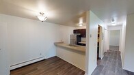 Located at 4636 Beech Ave in Kalamazoo, Michigan, this single-floor unit offers a practical and well-organized layout. The living area features dark hardwood-style flooring throughout and receives natural light through a large sliding glass door fitted with vertical blinds, which also provides outdoor access. A wall-mounted air conditioning unit and baseboard heating ensure year-round comfort.

The kitchen is efficiently designed with dark espresso cabinetry, light-toned countertops, and stainless steel appliances including a refrigerator and range. A peninsula with an integrated sink separates the kitchen from the living and dining area, creating an open, connected feel while maintaining distinct functional zones. Additional counter space and upper cabinetry provide ample storage.

The bedroom is carpeted for warmth and comfort, featuring a window with blinds that allows natural light and outdoor views. Baseboard heating is present here as well. A closet provides dedicated storage space within the room.

The bathroom includes a full tub-shower combination with tiled surround featuring a decorative accent border, a vanity with a light countertop and dark cabinetry, and a wall mirror. The overall design of the unit is clean and neutral, with white walls throughout creating a bright and move-in-ready environment.