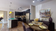 This single-story residence offers a thoughtfully designed layout that balances functionality with modern aesthetics. The kitchen serves as a standout feature, showcasing dark espresso cabinetry that extends to the ceiling, granite countertops, stainless steel appliances, and a mosaic tile backsplash in warm earth tones. Rich hardwood-style flooring runs throughout the kitchen and flows into the adjacent dining area, where a round table sits comfortably beneath track lighting. The living room features a bold accent wall, hardwood-style flooring, and a sliding glass door that opens to an outdoor area, allowing natural light to fill the space.

The bedrooms are carpeted for comfort and each includes windows with blinds and drape treatments, ceiling fans, and walk-in or reach-in closet access. The primary bedroom is generously proportioned and well-lit by natural light. Two bathrooms mirror the kitchen's design language, featuring dark vanity cabinetry, granite countertops, and hardwood-style flooring. One bathroom includes a walk-in glass shower, while the other offers a full soaking tub with a tiled surround, both finished with clean, neutral tiling.