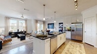 This single-story residence offers a thoughtfully designed open-concept floor plan that seamlessly connects the kitchen, dining, and living areas into one cohesive entertaining space. The kitchen serves as the centerpiece, featuring a large island with dark granite countertops, white cabinetry, stainless steel appliances, a tile backsplash, and pendant lighting that adds a polished, contemporary feel. Bar seating at the island connects directly to the adjacent dining and living areas, enhancing the home's social flow.

The living area is bright and welcoming, bathed in natural light through large windows dressed with sheer curtains. The primary bedroom is generously sized, showcasing a dramatic dark accent wall, a ceiling fan, multiple windows with outdoor views, and direct access to a private balcony. Its en-suite bathroom features a long dark granite vanity, white cabinetry, and ample storage. Additional bedrooms are well-proportioned and share access to the remaining bathrooms, each finished with clean white fixtures and consistent design details.

Throughout the home, polished concrete flooring adds a modern, durable foundation, while ceiling fans in key rooms contribute to comfort. A dedicated closet provides organized storage, completing this stylish and functional residence.