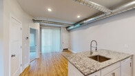 This two-story unit in Clawson, Michigan offers a distinctive industrial-chic aesthetic across four bedrooms, two bathrooms, and a loft. The main floor sets an open, airy tone with smooth hardwood flooring, recessed lighting, and a striking kitchen featuring white shaker cabinetry, granite countertops, a peninsula with an undermount sink and commercial-style faucet, and exposed metallic ductwork that adds a bold architectural character to the space. A large sliding glass door floods the living area with natural light. The bathrooms are finished with white vanities, hardwood flooring, and clean, neutral tiling, with one featuring a soaking tub and shower combination. Upper-level bedrooms are carpeted in neutral tones, offering a comfortable, quiet retreat. The generously sized primary bedroom includes access to a loft space, providing additional flexible square footage. Secondary bedrooms feature wide windows with outdoor views, inviting ample natural light. Neutral wall tones throughout create a clean, cohesive canvas. The loft adds a versatile bonus area ideal for a home office or lounge. This well-appointed multi-level home balances modern finishes with industrial design elements for a truly unique living experience.