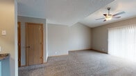 This two-floor residence offers a practical and functional layout designed for comfortable everyday living. The main level centers around a spacious open living area with soaring vaulted ceilings and a ceiling fan, creating an airy, open atmosphere. A sliding glass door floods the living space with natural light while providing outdoor access. The kitchen is situated adjacent to the living area and features warm oak cabinetry, dark granite-style countertops, a tile backsplash, a double stainless steel sink, and black appliances including a refrigerator and electric range. A staircase connects the main level to the upper floor, where multiple carpeted bedrooms are found. Each bedroom is finished with neutral-toned walls, warm oak door trim, and plush carpet underfoot. One bedroom features a ceiling fan, while another benefits from a bright window with blinds and access to a closet. Throughout the home, consistent warm oak baseboards and door trim provide a cohesive design detail. The full bathroom is appointed with tile flooring in an earthy stone pattern, a vanity with storage, a toilet, and a tub-shower combination. Textured ceilings are present throughout, and the overall palette of warm neutrals creates a calm, understated ambiance across both levels.