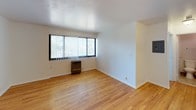 Seaway Terrace presents a thoughtfully laid out 1-bedroom, 1-bathroom single-floor residence designed for comfortable everyday living. The open living area is finished with warm, light-toned hardwood flooring that extends throughout the main spaces, creating a cohesive and inviting atmosphere. A large window fitted with vertical blinds allows natural light to fill the room while offering views of the surrounding greenery outside.

The kitchen is efficiently designed and tucked into its own dedicated nook, featuring warm wood cabinetry, dark granite-style countertops, a stainless steel single-basin sink, a gas range, and a full-size refrigerator. Tile flooring in the kitchen provides a practical transition from the hardwood living areas.

The bathroom is clean and functional, equipped with a wood-trimmed vanity, a wall-mounted medicine cabinet mirror, and a full bathtub and shower combination with tile surround. Tile flooring and a lighted vanity bar complete the space.

The bedroom offers a comfortable footprint with the same hardwood flooring found throughout, and the floor plan also includes closet space for storage. The overall layout is efficient and straightforward, making this residence a practical and well-maintained option at Seaway Terrace.