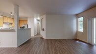 Located at 14719 Main St, Unit G208 in Mill Creek, WA, this 3-bedroom, 2-bathroom apartment delivers 1,160 square feet of comfortable single-floor living. Wood-style flooring flows throughout the unit, complementing the neutral palette and clean lines found in every room. The open living area centers around a fireplace with an arched decorative surround and connects to a private balcony through sliding glass doors, bringing in natural light and tree-lined views. The kitchen features warm honey-toned cabinetry, light stone countertops, a peninsula with a sink, and stainless steel appliances including a gas range and refrigerator, with track lighting overhead. The primary bedroom spans 150 square feet and includes access to a dedicated walk-in closet outfitted with wire shelving on multiple walls and wood-style flooring. Additional bedrooms offer ample space and large windows with views of surrounding greenery. The two bathrooms include a tub-shower combination with a brushed nickel towel bar. A dedicated laundry room houses a full-size washer and dryer with overhead wire shelving for added storage. This well-appointed apartment balances functional layout with comfortable finishes throughout.