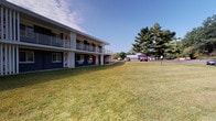 Located at 3946 Fishcreek Rd in Stow, Ohio, this single-floor unit is part of a two-story multi-unit building with a classic blue and white exterior facade. The building is set against a well-kept, open lawn with mature evergreen trees, providing a pleasant and spacious outdoor environment with ample parking nearby.

Inside, the unit features warm hardwood-style flooring and neutral gray walls that create a clean, cohesive aesthetic throughout. Interior doors are finished in white with paneled detailing and brushed nickel lever hardware, contributing a polished, modern touch.

The bathroom is thoughtfully appointed and serves as a functional highlight of the unit. It includes a dark-cabinet vanity topped with a white solid-surface countertop and an undermount sink paired with chrome fixtures. A large mirror above the vanity reflects the well-lit space, enhanced by a multi-bulb vanity light fixture. Towel ring hardware in chrome adds a refined detail. The bathroom also features a shower and tub combination enclosed by a decorative patterned curtain, a toilet, and durable hardwood-style flooring that runs throughout. Neutral gray walls keep the space feeling bright and open.

Overall, the unit presents a clean, updated living environment with consistent finishes, practical amenities, and access to the serene outdoor surroundings of Stow, Ohio.