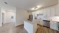 Located at 6104 Vintage Brunswick Cir in Brunswick, Georgia, this single-story, three-bedroom, two-bathroom home offers a well-designed layout with modern finishes throughout. Wood-look flooring flows consistently across the living areas and bedrooms, lending a cohesive, contemporary feel to the space.

The kitchen is a standout feature, showcasing white shaker cabinetry, a classic subway tile backsplash, granite countertops, and stainless steel appliances including a refrigerator and dishwasher. A central kitchen island provides additional prep space and opens naturally toward the living area, creating an inviting, open-concept flow.

The bedrooms are bright and well-proportioned, each equipped with a ceiling fan and windows that bring in natural light. The spacious primary bedroom includes its own closet with wire shelving. A total of three closets offer ample storage throughout the home.

The bathrooms are finished with granite-topped vanities, white cabinetry, and tile flooring. The primary bathroom features a glass-enclosed walk-in shower. A dedicated laundry room with side-by-side washer and dryer hookups adds everyday convenience.

A hallway with built-in shelving provides additional display or storage space, and the clean, neutral palette throughout gives the home a bright, move-in-ready appeal.