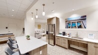 Located at 901 N Market St in the heart of Wilmington, Delaware, this contemporary amenity space delivers a polished, multi-functional environment designed for both relaxation and collaboration. The single-floor layout is organized into several distinct yet interconnected zones, each thoughtfully appointed with modern finishes throughout.

The kitchenette area serves as a central hub, featuring warm wood-toned cabinetry, a stainless steel full-size refrigerator, a subway tile backsplash, a single-basin sink, and a coffee station. A white quartz island with bar seating anchors the space, illuminated by a series of pendant lights that add a refined touch.

Adjacent to the kitchenette, a comfortable lounge area offers plush neutral sofas, a wall-mounted flat-screen television, and a media console — ideal for casual gatherings or informal meetings. Recessed lighting and light-toned carpet keep the atmosphere bright and welcoming.

A second lounge zone features coordinating neutral seating and opens into a striking communal area defined by bold geometric structural columns and exposed brick walls visible through floor-to-ceiling glass partitions. This area also includes a pool table, adding a recreational element to the space.

The glass-enclosed room beyond the partitions provides a more private setting suitable for meetings or events. Throughout the space, curated artwork referencing local Wilmington architecture reinforces a strong sense of place and community identity.
