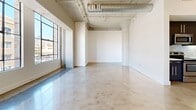 Located in the heart of Downtown Los Angeles at 217 E 8th St, this urban loft-style unit embodies the industrial-chic aesthetic characteristic of the neighborhood. The open-plan main living area is defined by gleaming polished concrete floors that reflect natural light streaming in through large, steel-framed industrial windows overlooking the city streetscape. Exposed ductwork and raw concrete ceilings overhead reinforce the loft's warehouse-inspired character, while crisp white walls provide a clean, versatile backdrop throughout the space.

The kitchen is thoughtfully designed with sleek dark cabinetry, a classic subway tile backsplash, and a full suite of stainless steel appliances including a refrigerator with ice maker, electric range, built-in microwave, and dishwasher. The layout flows efficiently, making the kitchen both functional and visually cohesive with the open living area.

The bathroom offers a refined contrast to the raw industrial elements found elsewhere. It features a soaking tub with a glass enclosure, floor-to-ceiling penny mosaic tile in soft grey tones, polished chrome fixtures, and wall-mounted lighting — creating a spa-like retreat within the unit.

Track lighting and exposed conduit add finishing industrial touches, making this Downtown LA loft a compelling blend of raw urban character and modern amenities.